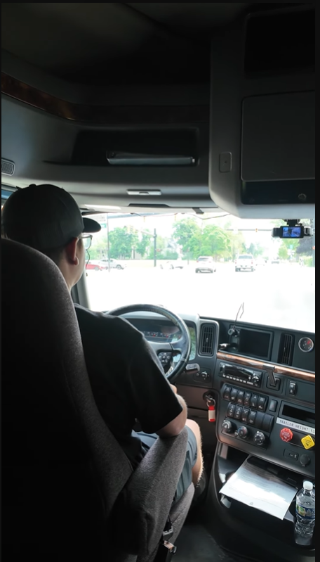 CDL student driving an Alpha Omega training truck, hands on the wheel approaching an intersection